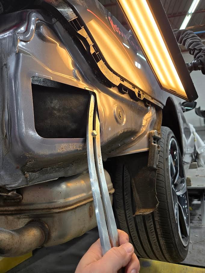 PDR technician working behind a car panel with dent repair tools